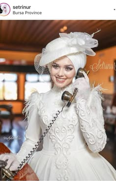 a woman in a white dress is talking on the phone while wearing a veil and gloves