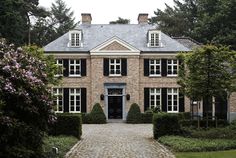 a large brick house with black shutters on the front door and windows, surrounded by trees