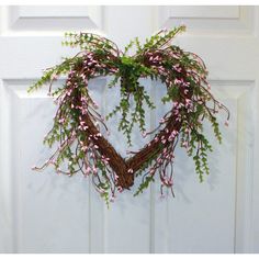 a heart shaped wreath with pink flowers hanging from the front door, on a white door