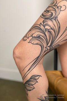 a woman's legs with tattoos on them sitting in a chair next to a wall