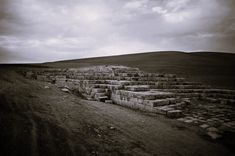 an old stone structure sitting in the middle of a grass covered field under a cloudy sky