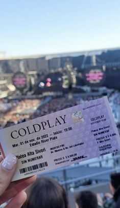 a person holding up a ticket for coldplay in front of a crowd at a concert