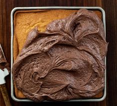 chocolate frosting on top of a cake in a pan next to a spatula