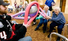 an elderly man is playing with inflatable balls while others watch from the waiting room