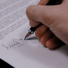 a hand holding a pen and writing on a piece of paper that has been signed