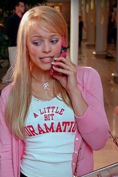 a woman talking on a cell phone while wearing a pink cardigan and white t - shirt