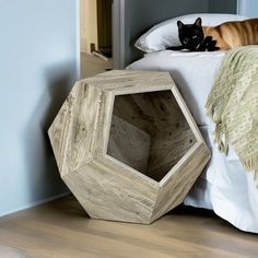 a cat laying on top of a white bed next to a wooden box shaped like an octagon