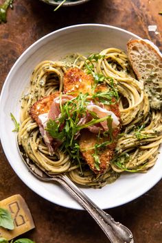 a white bowl filled with pasta and meat on top of a wooden table next to bread