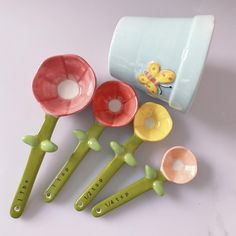 four ceramic measuring spoons with flowers in them and a cup on the side that says help