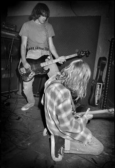 two young men playing guitars in a recording studio, one is kneeling down and the other is standing up