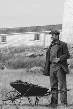 a man standing next to a wheelbarrow with a house in the back ground