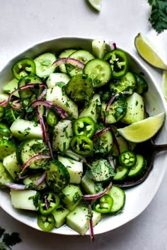 a white bowl filled with cucumbers, onions and cilantro on top of a table