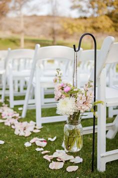 an outdoor ceremony with white chairs and flowers in vases on the aisle, along with petals scattered all over the grass