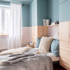 a bed sitting next to a window in a room with blue walls and white curtains