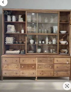 an old wooden cabinet with glass doors and shelves filled with dishes, cups, and vases