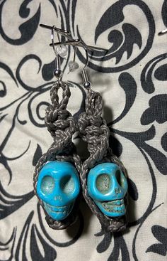 a pair of blue and gray skull earrings on a black and white fabric with silver hooks