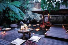 a deck with candles and pillows on it next to a table in the middle of some water