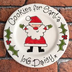 a white plate with a drawing of santa clause on it's face and words that say cookies for santa love daisy