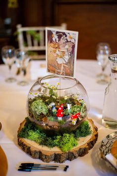 a glass bowl filled with plants on top of a wooden slice next to a table