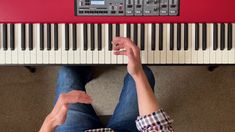 a person sitting on the floor next to a red piano and playing it with their fingers