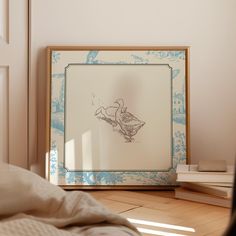 a framed drawing is sitting on the floor next to some books and a bed in a room