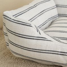 a white and black striped pillow sitting on top of a carpeted floor next to a wall