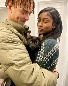 a man holding a cat in his arms while standing next to a woman with dreadlocks