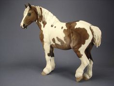 a brown and white horse figurine standing on a gray surface with its head turned to the side