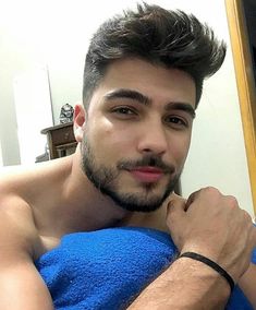 a shirtless man in a blue towel looking at the camera with his hand on his chest