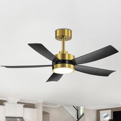 a ceiling fan with two black blades and a gold light fixture in a white room