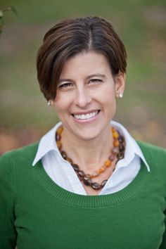 a woman wearing a green sweater smiles at the camera