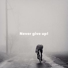 a man riding a bike down a foggy road with the words never give up