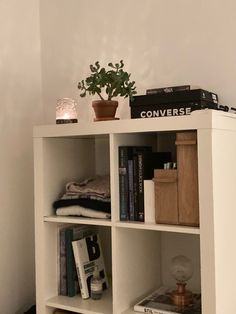 a white book shelf with books and plants on top