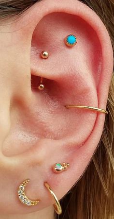 a woman wearing three different ear piercings on her left ear and one with a turquoise stone in the middle