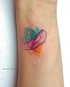 a heart tattoo on the wrist with watercolor splashes and an abstract shape in the center