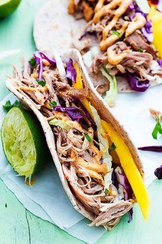 two pulled pork tacos with cole slaw and lime wedges on the side