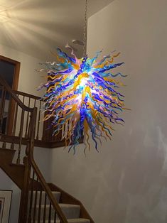 a colorful chandelier hanging from the ceiling in a room next to a stair case