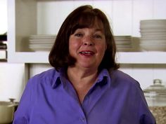 a woman standing in a kitchen with plates stacked on the shelves behind her