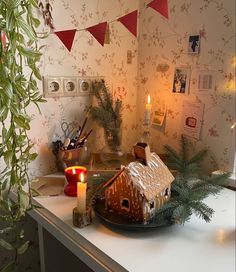 a gingerbread house on a plate with candles in front of it and christmas decorations hanging from the ceiling