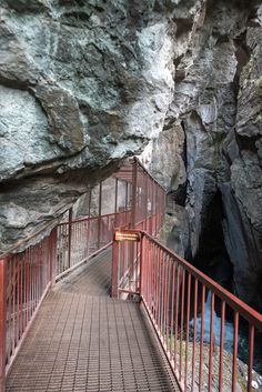 a wooden walkway leading to a cave with red railings and a sign on it