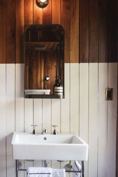 a white sink sitting under a mirror in a bathroom next to a wooden paneled wall