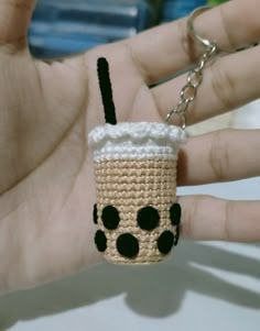 a crocheted coffee cup keychain with a black nose and eyes on it