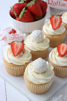 some cupcakes with white frosting and strawberries in the bowl behind them