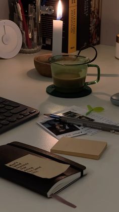 a desk with a computer keyboard, mouse and book on it next to a lit candle