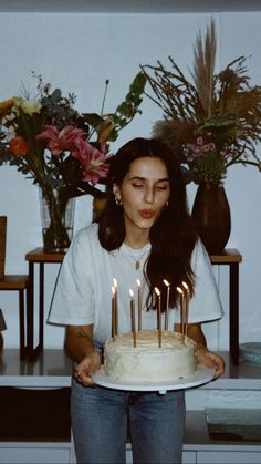 a woman standing in front of a cake with lit candles on it and flowers behind her