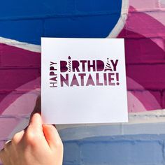 someone holding up a piece of paper with the words happy birthday natalie on it in front of a colorful wall