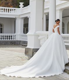 a woman in a white wedding dress standing on the steps near some pillars and columns