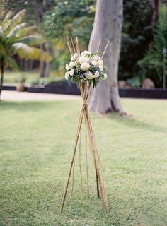 a wooden stand with flowers on it in the middle of a lawn next to a tree