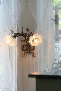 a wall light with three lights on it in front of a white curtained window