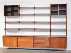 a wooden bookcase with drawers and shelves on the front, against a white wall